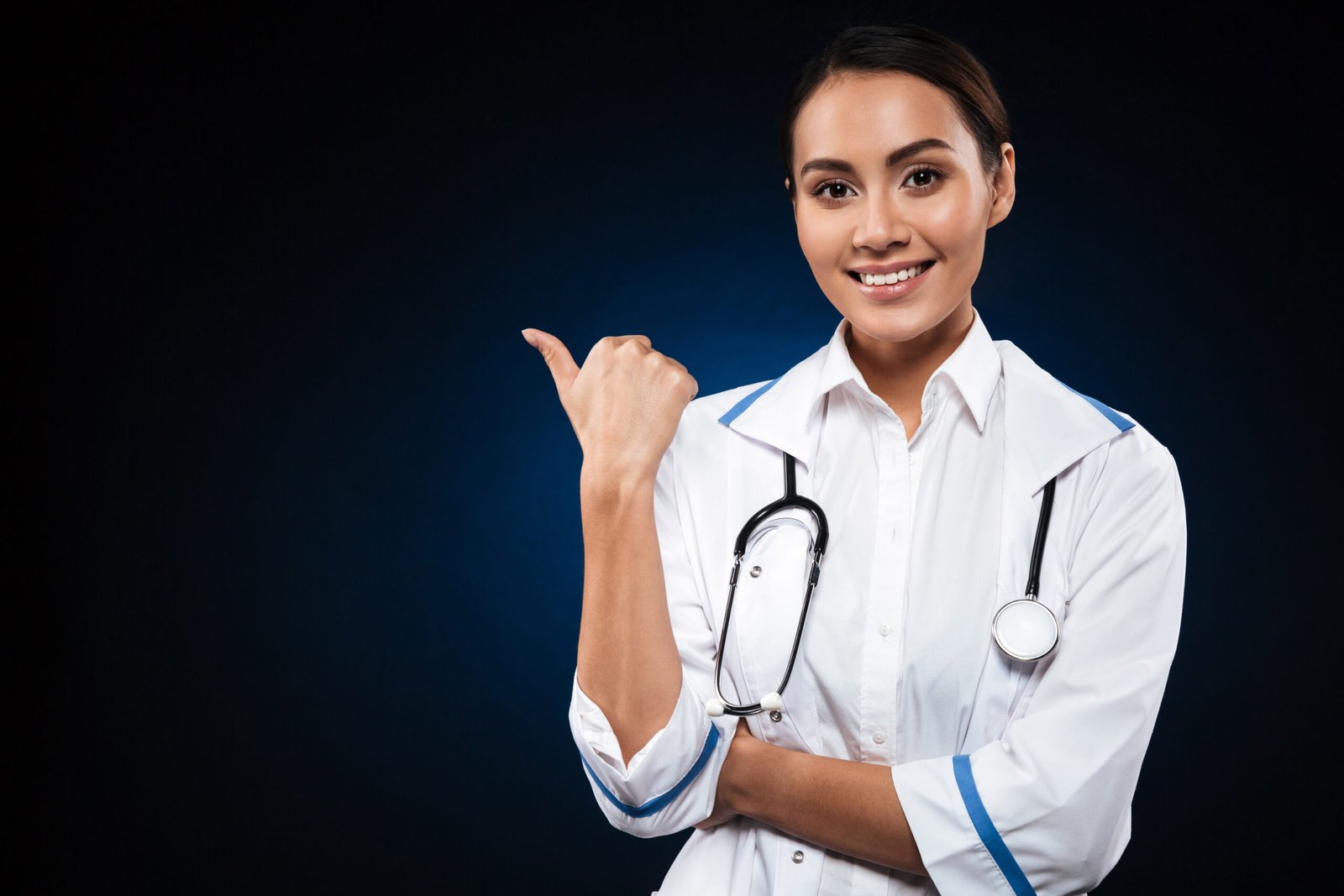 Young happy lady with stethoscope looking camera and pointing at copy space isolated over black